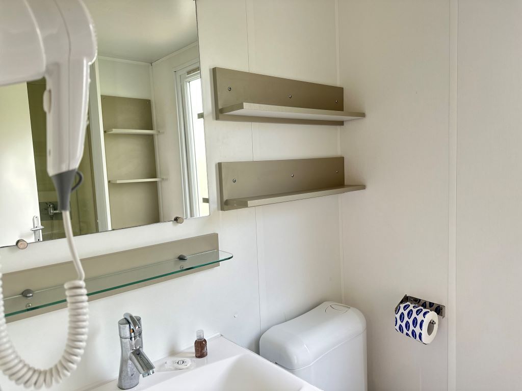 A bathroom with a white sink, a mirror, a hairdryer, and two beige shelves.