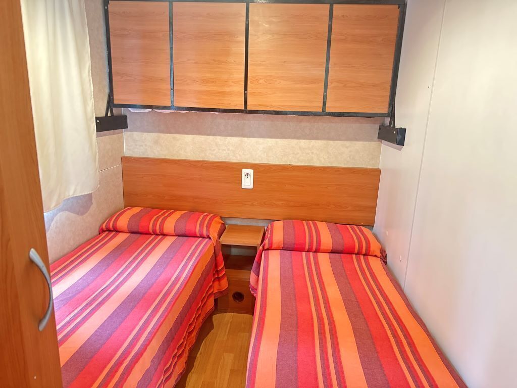 A compact RV bedroom with two beds, a wooden headboard, and a small table.