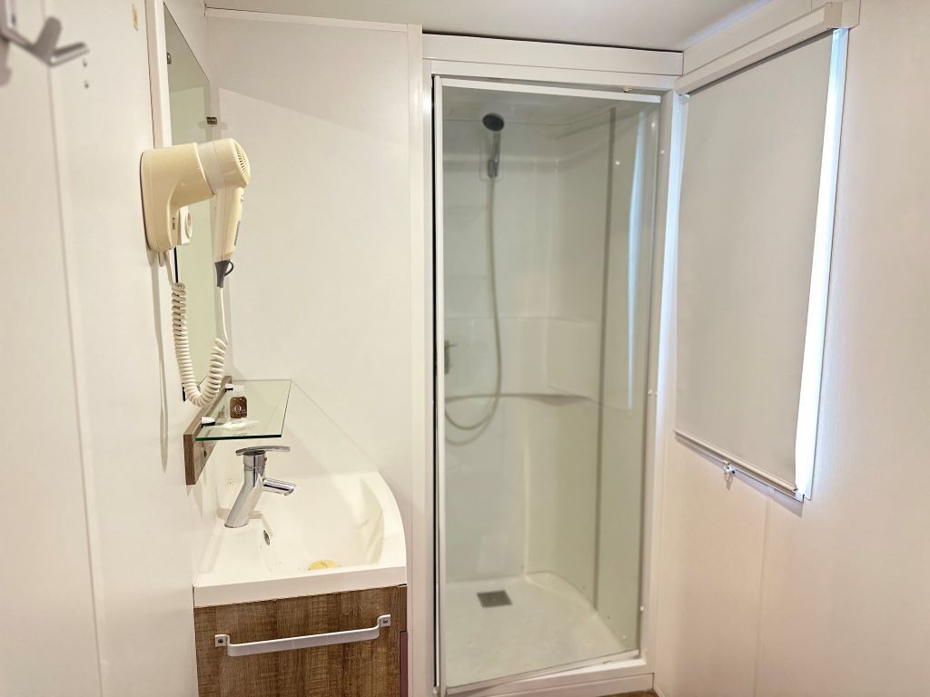 Ein modernes Badezimmer mit Duschkabine aus Glas, einem weißen Waschbecken mit Glasplatte und einem an der Wand befestigten Föhn.