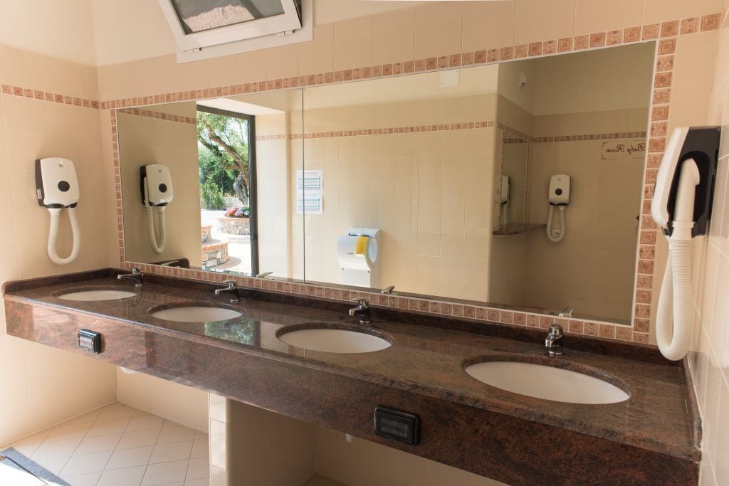 Une salle de bain avec trois lavabos, un grand miroir et un sèche-mains.