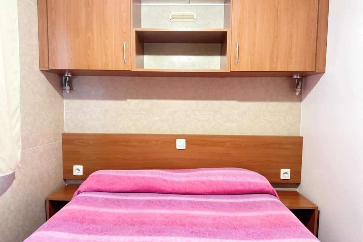 A bedroom with a wooden headboard, a bed with a pink striped blanket, and a small wooden nightstand.