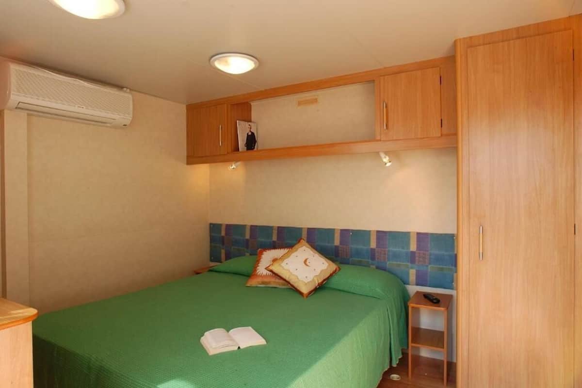 A single bed with a green bedspread, a nightstand with a remote control, and a wooden wardrobe.
