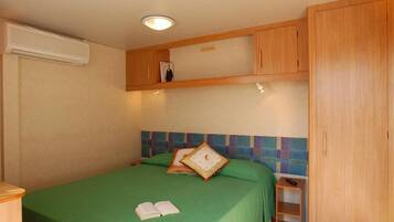 Un lit simple avec une couvre-lit verte, une table de chevet avec une télécommande et une armoire en bois.