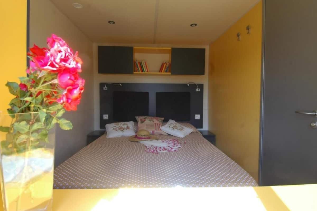 A bedroom with a bed, a bedside table, a vase with flowers, and a bookshelf.