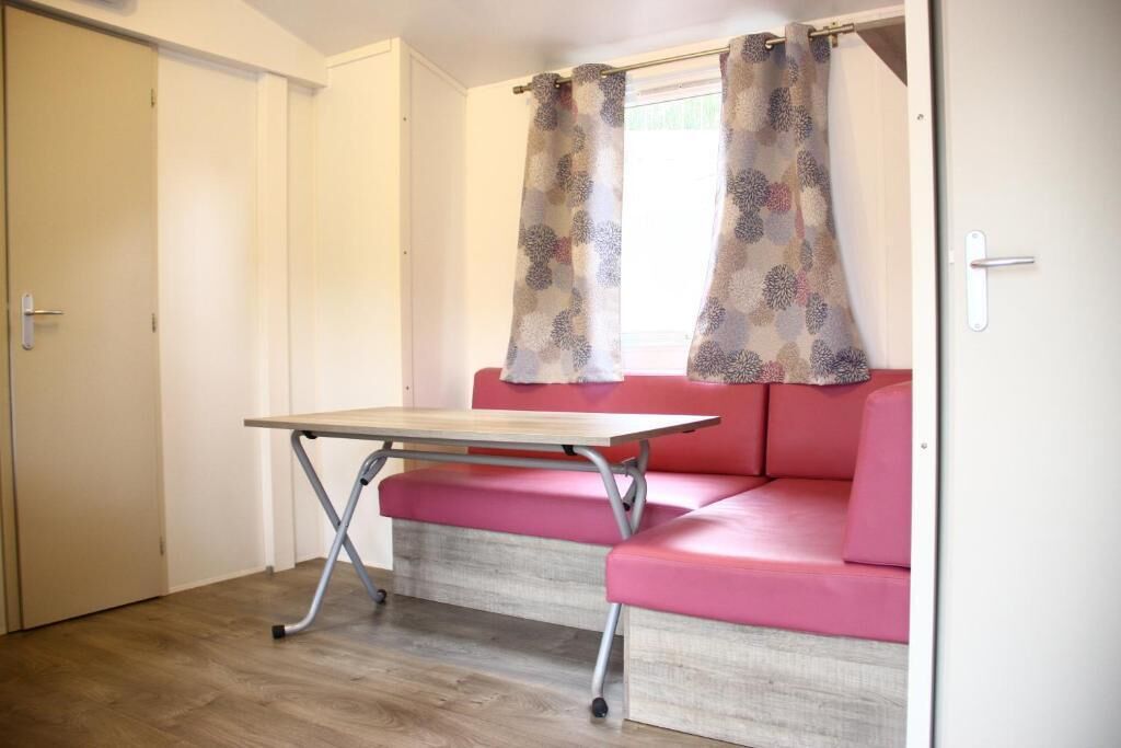 A room with a wooden floor, a pink sofa, a small table, and a window with patterned curtains.