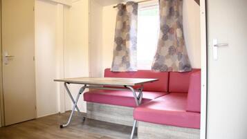 A room with a wooden floor, a pink sofa, a small table, and a window with patterned curtains.
