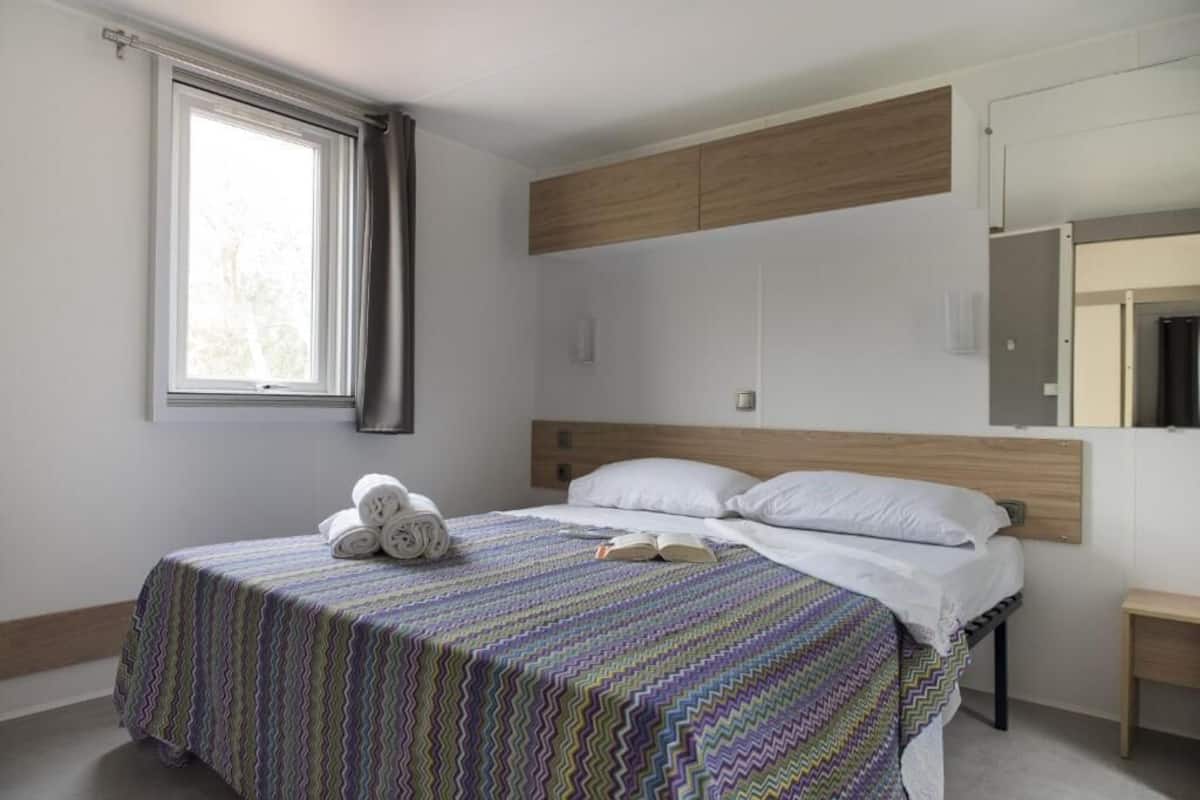 A bedroom with a bed, a window, a bedside table, and a mirror.