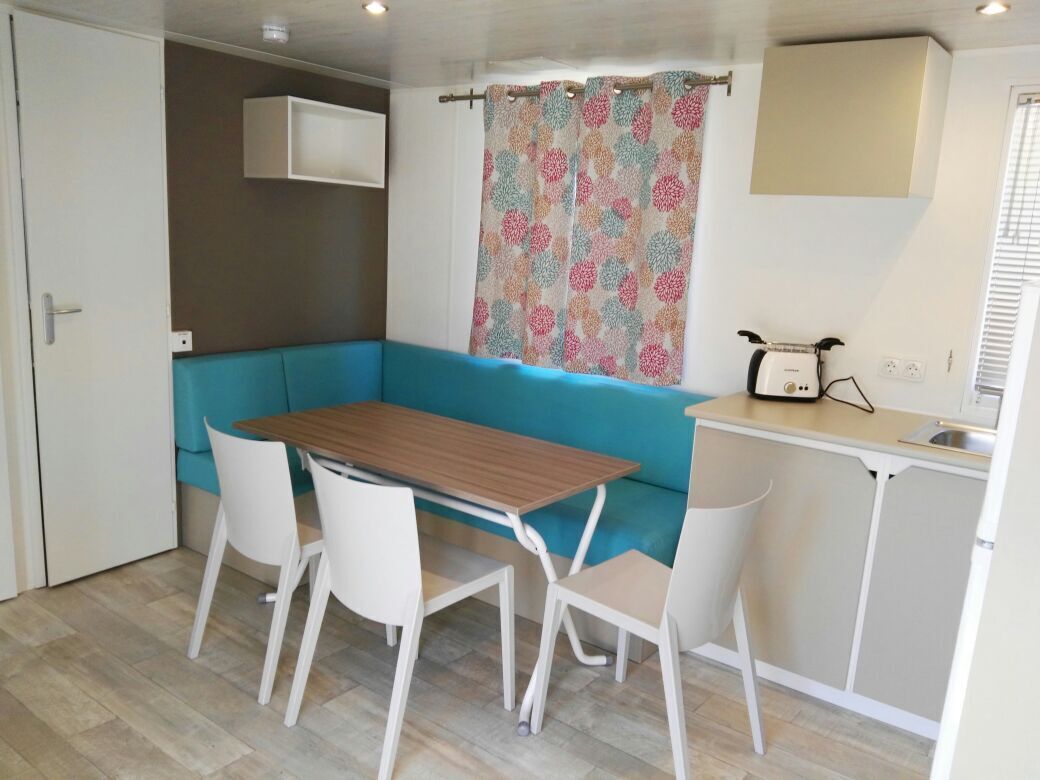Una kitchenette compacta con un sofá azul, una mesa de madera y sillas blancas.
