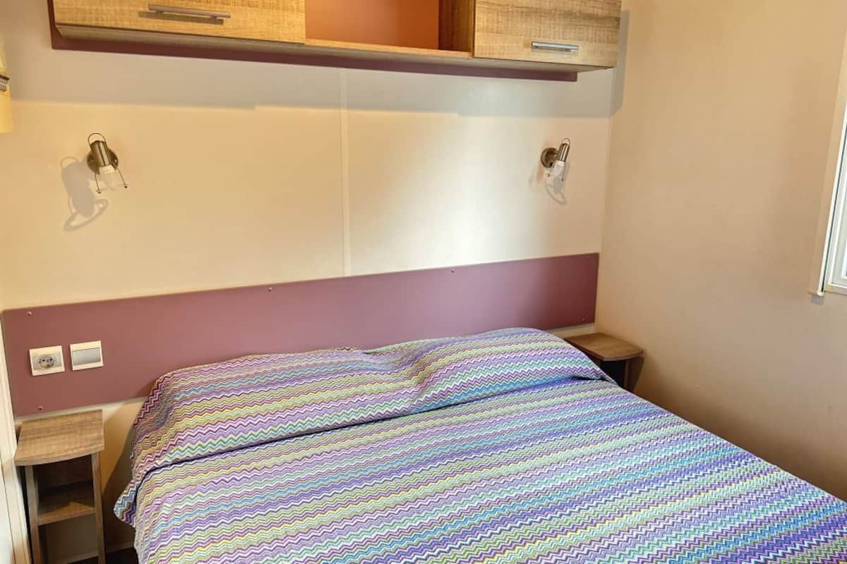 A single bed with a colorful zigzag patterned bedspread, a wooden headboard, and a small bedside table with a lamp.