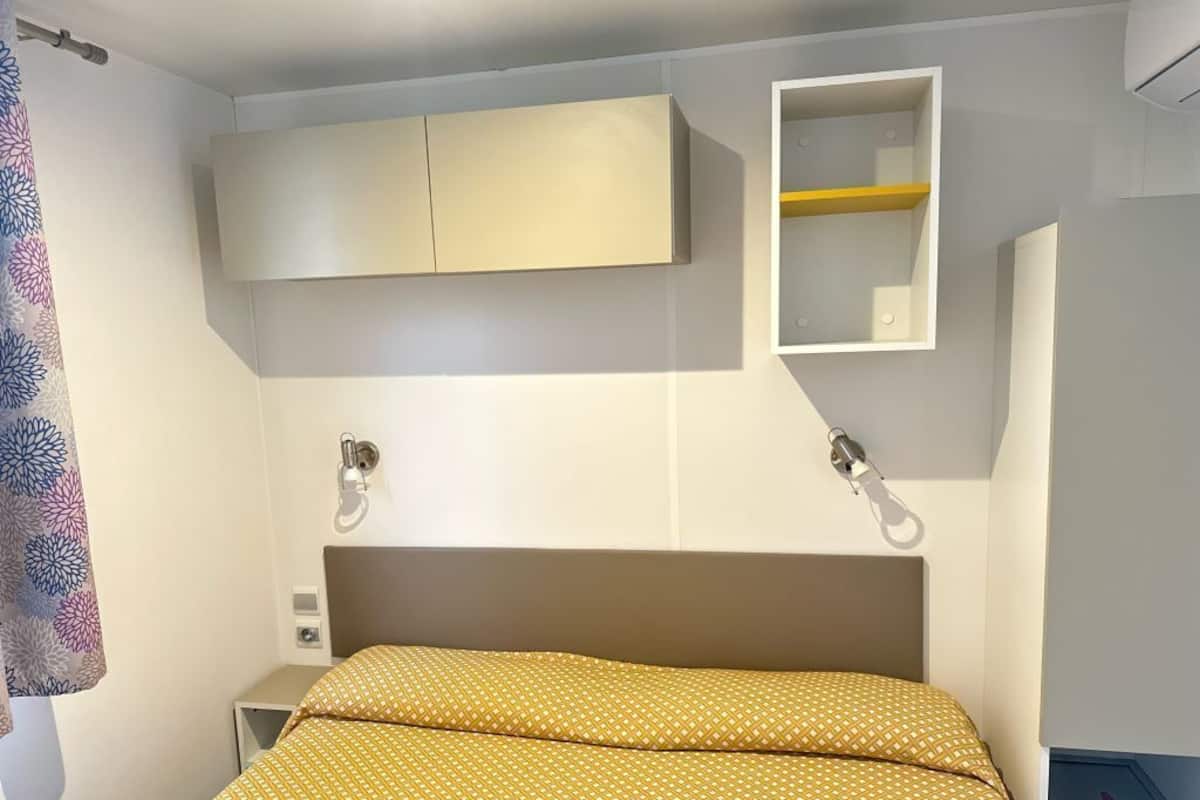 A hotel room with a bed, a wardrobe, a mirror, and a small shelf.