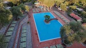 Vista aérea de un hotel con una piscina central, rodeado de sillas de descanso y un muro de piedra.