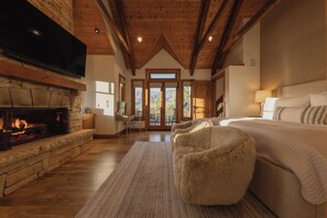 A bedroom with a fireplace, a large bed, and a view of the outdoors. - Modern Cabin by InvitedHome | Vast Patio, Fireplaces, Steps to Ski (Mountain Village)