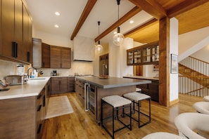 Una cocina moderna con armarios de madera, una isla grande con taburetes, iluminación colgante y una escalera a la vista.