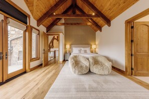 A bedroom with a wooden ceiling, a large bed with fluffy pillows, a stone wall, and a wooden door.