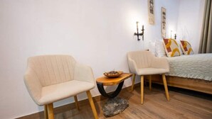 A room with two chairs, a small round table with a bowl, and a bed with a white quilt. - Casa Maya Transylvania Studio (Sighișoara)
