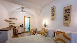 A compact hotel room with a bed, a desk, a chair, and a kitchenette. - Casa Maya Transylvania Studio (Sighișoara)