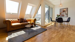 A modern living room with a sofa, coffee table, and dining area. - Grand Quarters City Residence (Vienna)