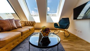 A modern living room with a leather sofa, a glass coffee table with fruit, a rocking chair, and skylights. - Grand Quarters City Residence (Vienna)
