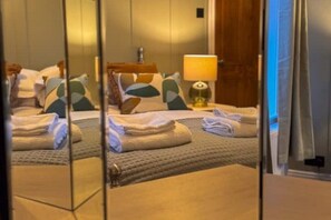 Een hotelkamer met een bed, kussens, een lamp en een spiegel die de kamer weerspiegelt.