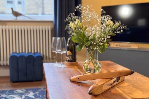 A wooden table with a vase of flowers, a wine glass, and a wooden spoon. - Beautiful, Relaxing Home in Central Saltaire (Saltaire)