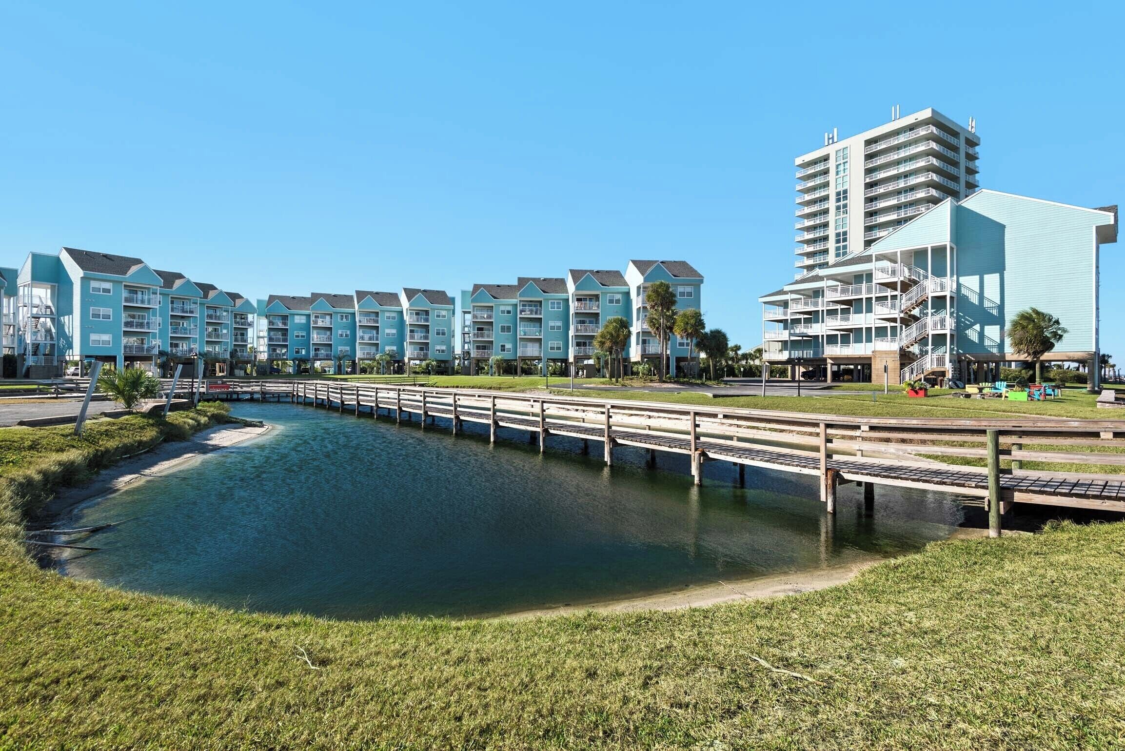 A waterfront property with a long wooden pier, a series of light blue buildings, and a tall structure with balconies.