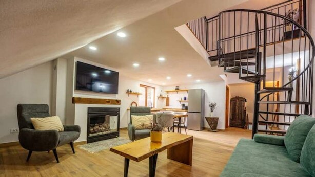 Un salon avec une cheminée, un canapé vert, une table basse en bois et un escalier en colimaçon.