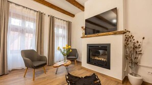 A living room with a fireplace, two armchairs, a coffee table, and a black leather sofa. - Casa Maya Transylvania Apartment (Sighișoara)