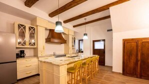 A kitchen with wooden beams, a central island with bar stools, and a refrigerator. - Casa Maya Transylvania Apartment (Sighișoara)