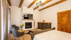 A bedroom with a bed, a TV mounted on the wall, a fireplace, and wooden beams on the ceiling. - Casa Maya Transylvania Apartment (Sighișoara)