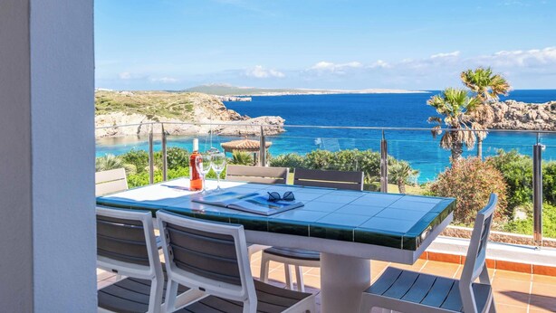 Terraza con mesa y sillas con vistas al mar, bajo un cielo despejado.