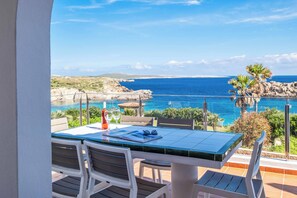 Une terrasse avec une table et des chaises donnant sur une vue côtière, sous un ciel dégagé.