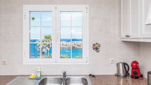 Una cocina con un lavamanos doble, una ventana con vistas al mar, un hervidor y una cafetera roja.