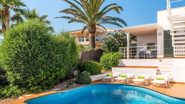 A swimming pool with lounge chairs, surrounded by greenery and a building with a balcony. - Es Llaut - Three Bedroom Villa, Sleeps 6 (Binibeca)