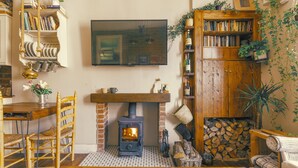 A cozy living room with a fireplace, wooden furniture, a TV mounted on the wall, and bookshelves filled with books and decorative items.