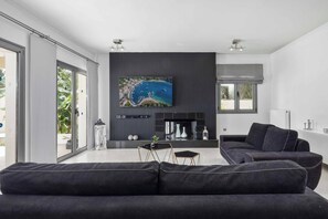A modern living room with a large flat-screen TV, a dark-colored sofa, and a glass door leading to an outdoor area.