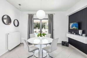 A modern dining area with a round table, chairs, a potted plant, and a TV on a black wall.