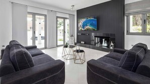 Un soggiorno moderno con una grande televisione a schermo piatto, divani scuri e un tavolino in vetro.