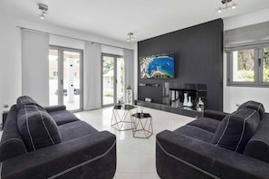 A modern living room with a large flat-screen TV, dark sofas, and a glass coffee table.