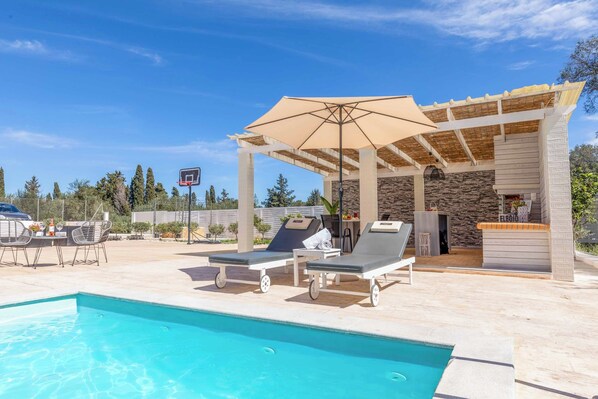 A pool area with lounge chairs, a covered seating area, and a bar.