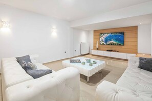 A modern living room with a white sofa set, a coffee table, and a flat-screen TV mounted on the wall.