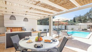 Patio esterno con tavolo rotondo, sedie, piscina e area coperta con barbecue.