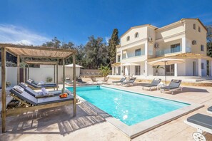 Ein Poolbereich mit Liegestühlen, einer Pergola und einem zweistöckigen Gebäude mit Balkonen.