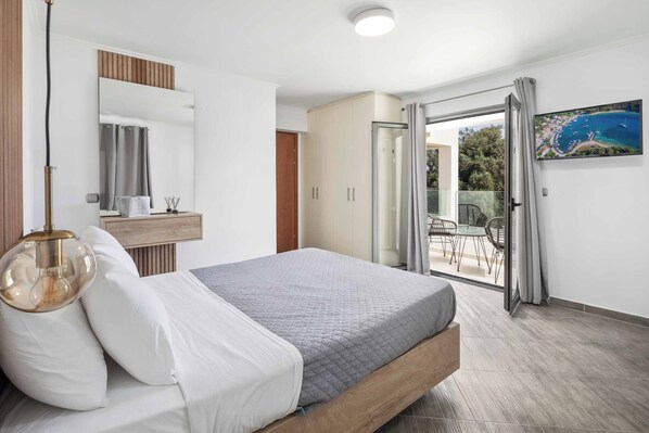 Ein Schlafzimmer mit einem Bett, einem Nachttisch, einem Spiegel, einem Kleiderschrank und Blick ins Freie.