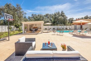 An outdoor patio with wicker furniture, a pool, and a covered seating area.