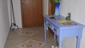 A hallway with patterned floor tiles, a wooden door, a blue table with decorative items, and a tall floor lamp. - Plus Couple Suite with mini kitchen (Ilhabela)