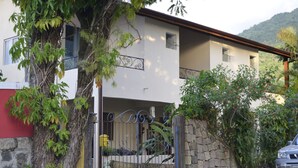 A two-story house with a stone wall and a metal gate. - Plus Couple Suite with mini kitchen (Ilhabela)