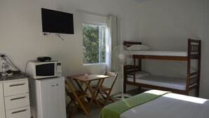 Ein kleines Zimmer mit einem Etagenbett, einem kleinen Schreibtisch mit einer Mikrowelle, einem Stuhl und einem Standventilator.