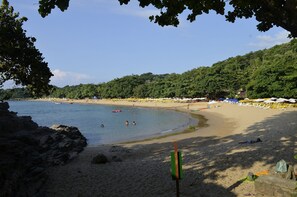 Ein Strand mit klarem Wasser, sandigem Ufer und einer bewaldeten Hügelkette im Hintergrund.
