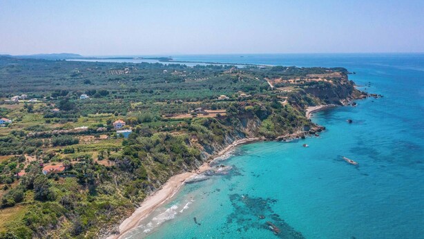 An aerial view of a coastal area with a beach, cliffs, and scattered buildings. - Villa Teo - Four Bedroom Villa, Sleeps 8 (Ionian Islands)