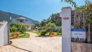 A villa entrance with a paved driveway, a wooden fence, and a sign indicating 'Villa Teo' and 'Solmar Villa Holidays'. - Villa Teo - Four Bedroom Villa, Sleeps 8 (Ionian Islands)